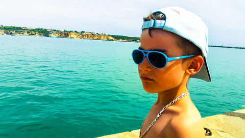 Shirtless boy in sunglasses at beach against sky