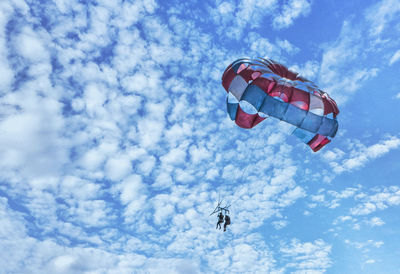 Low angle view of people paragliding against sky