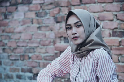 Close-up portrait of woman wearing hijab against brick wall