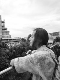 Side view of man looking at city buildings against sky