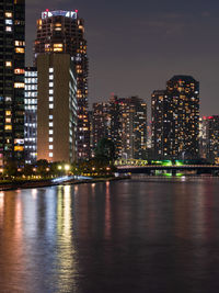 Illuminated buildings by river against sky at night