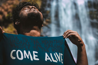 Close-up of man wearing t-shirt with text by waterfall