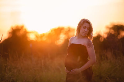 Full length of young woman touching grass during sunset