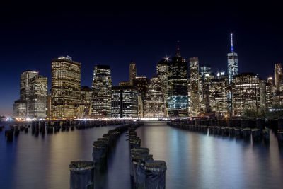 Illuminated buildings by river against sky at night