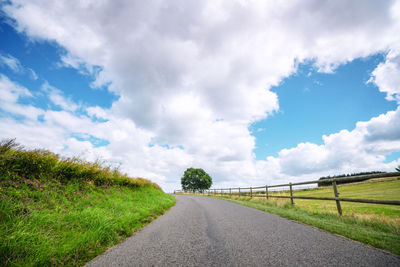 Empty road amidst field against sky