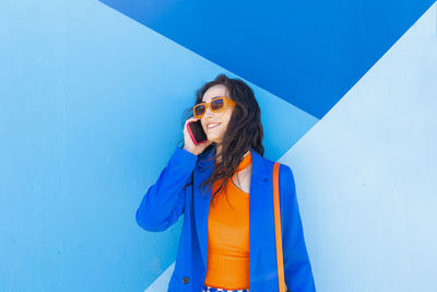 Young woman wearing sunglasses while standing against blue background