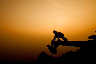 Silhouette people on cliff against sky during sunset