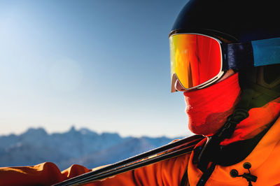 Portrait of a skier in profile in ski goggles against a clear blue sky and mountains