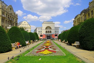 People in garden by buildings against sky