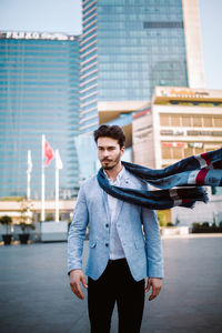 Portrait of young man standing against buildings in city