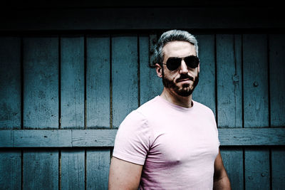 Portrait of young man wearing sunglasses standing against wall
