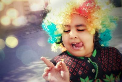 Playful boy wearing colorful wig sticking out tongue on road