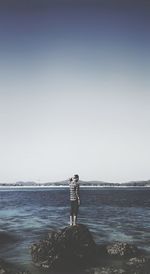 Man standing on rock at beach against clear sky