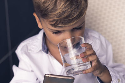 Boy drinking water while using phone at home
