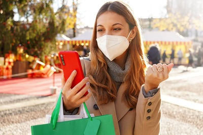 Young woman wearing mask while using mobile phone outdoors