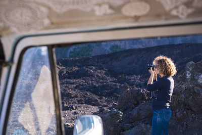 Woman photographing with camera seen through travel trailer's window