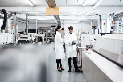 Male and female scientists discussing over laptop by machinery at laboratory