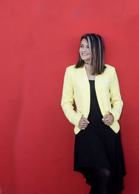 Happy young woman standing against red wall