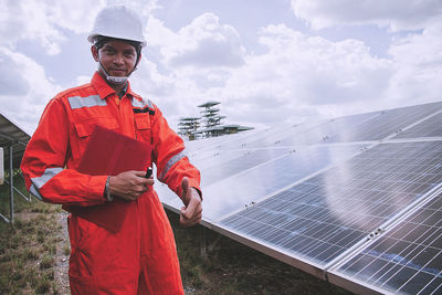 Portrait of worker wearing reflective clothing while standing on solar panel against sky