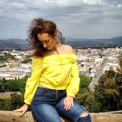 Young woman in yellow top sitting at observation point against sky