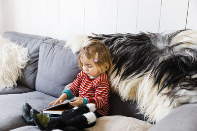 Cute girl looking at book while sitting on sofa