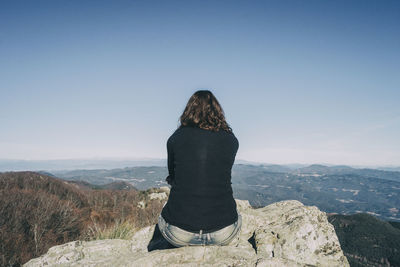 Girl from the back sitting on a top stone looking at the distant mountains