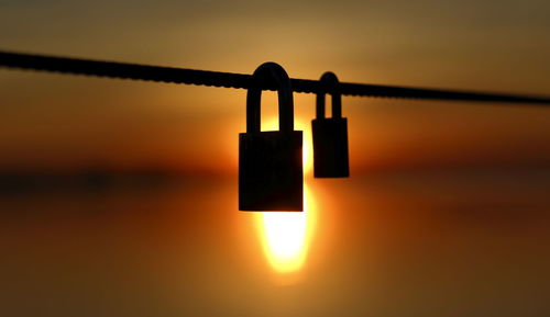 Close-up of silhouette love lock hanging on string by lake against sky during sunset