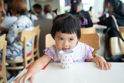 Cute girl licking cup while sitting at cafe