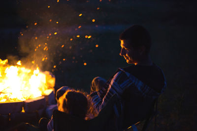 Dad and daughter sit at night by the fire in the open air in the summer in nature. family camping 