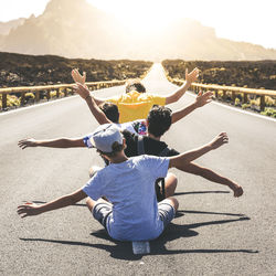 Rear view of people with arms outstretched sitting on road