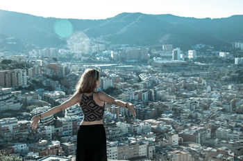 Woman standing with arms outstretched by cityscape and mountains