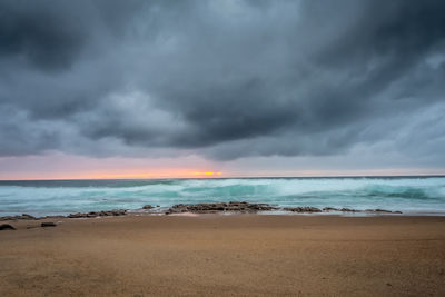 Scenic view of beach and sea against dramatic cloudy sky