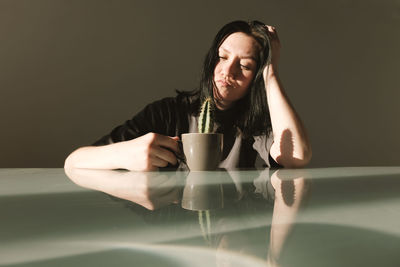 Young upset woman in a gray t-shirt holds in her hands a coffee cup with a cactus