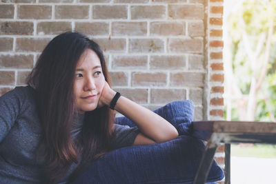 Portrait of a young woman sitting against brick wall