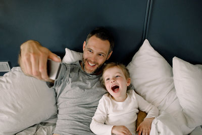 High angle view of father taking selfie with daughter on bed in hotel