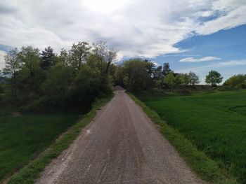 Empty road amidst trees against sky