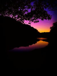 Silhouette trees by lake against sky at night