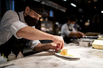 Chef garnishing pudding while standing in restaurant kitchen