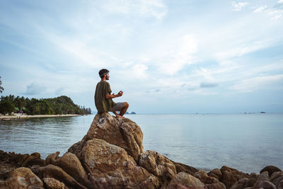 Man sitting on rock by sea against sky