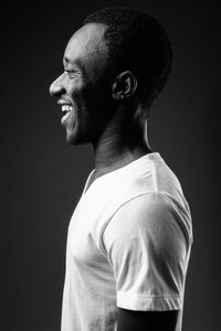 Side view of young man looking away against black background