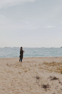 Side view of mid adult woman standing at beach against sky