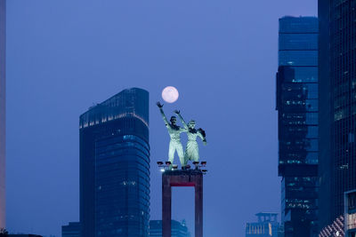 Low angle view of statues against clear sky in city at dusk