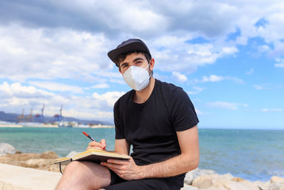 Young man holding sunglasses against sky