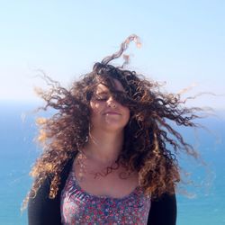 Young woman with tousled hair against sky