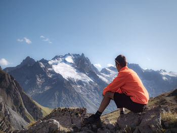 Man sitting on rock by mountains against sky