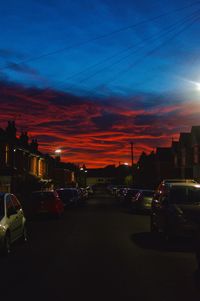 Cars on street by buildings against sky at night