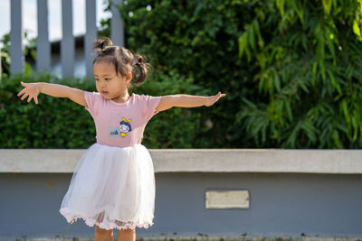 Girl with arms outstretched standing against plants