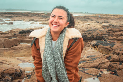 Portrait of smiling young woman standing on rock at beach