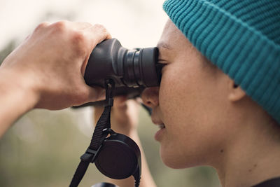 Side view of woman looking through binoculars in forest