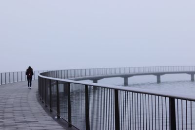 Rear view of woman walking on footbridge over sea against sky